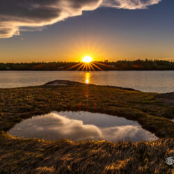 Sun setting across calm water with reflections in a tidal pool at Stockbridge Point in Freeport, Maine