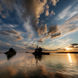 photo of a sunset over the water with a boat and island in the scene along with moody clouds