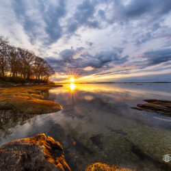Sunrise reflections and dramatic clouds along the shoreline at Winslow Park in Freeport, Maine