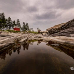 Reflection of Pemaquid Point Lighthouse in a tide pool surrounded by rocky ledges in Bristol, Maine.